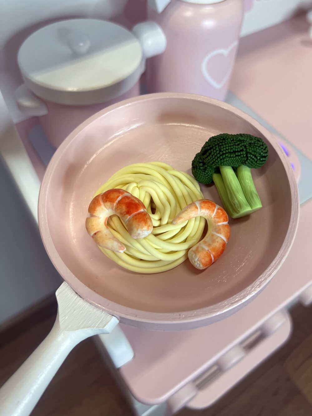 На детской игровой сковороде лежит 2 креветки, спагетти и брокколи