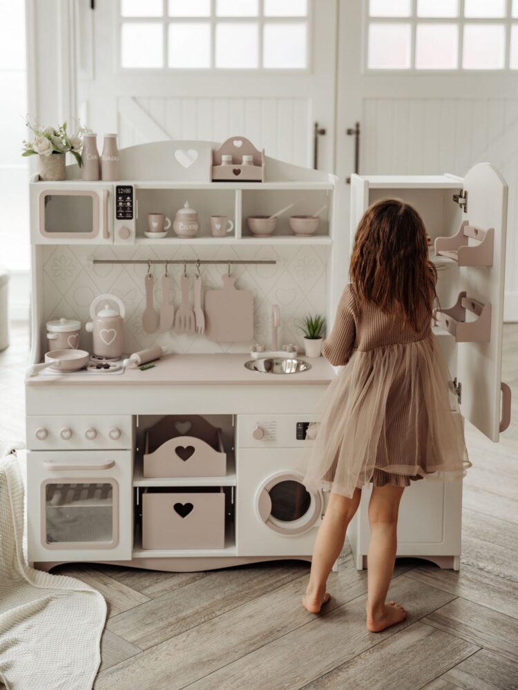 Девочка в коричневом платье достаёт продукты из игрушечного холодильника, чтобы приготовить кулинарный изыск. Общий вид.
