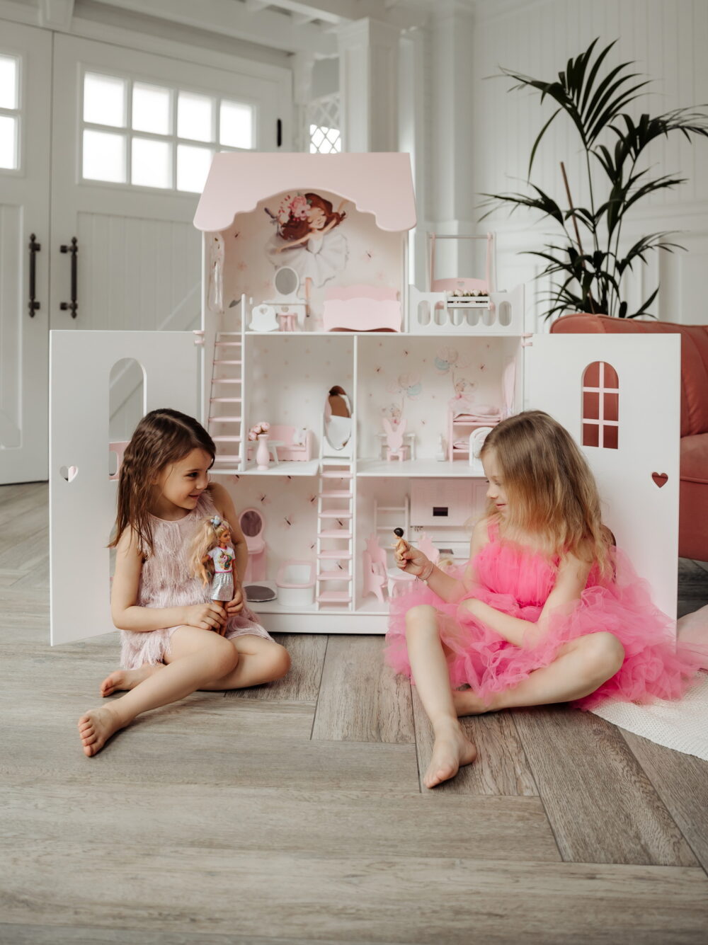 Красивый кукольный домик с дверями, две подруги играют в куклы. На домике нарисованы милые зайки. Вид с открытыми дверками.