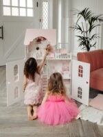 Красивый кукольный домик с дверями. Две подруги увлеченно играют в куклы. На домике нарисованы милые зайки. Вид с открытыми дверками, внутри лежит кукла барби.